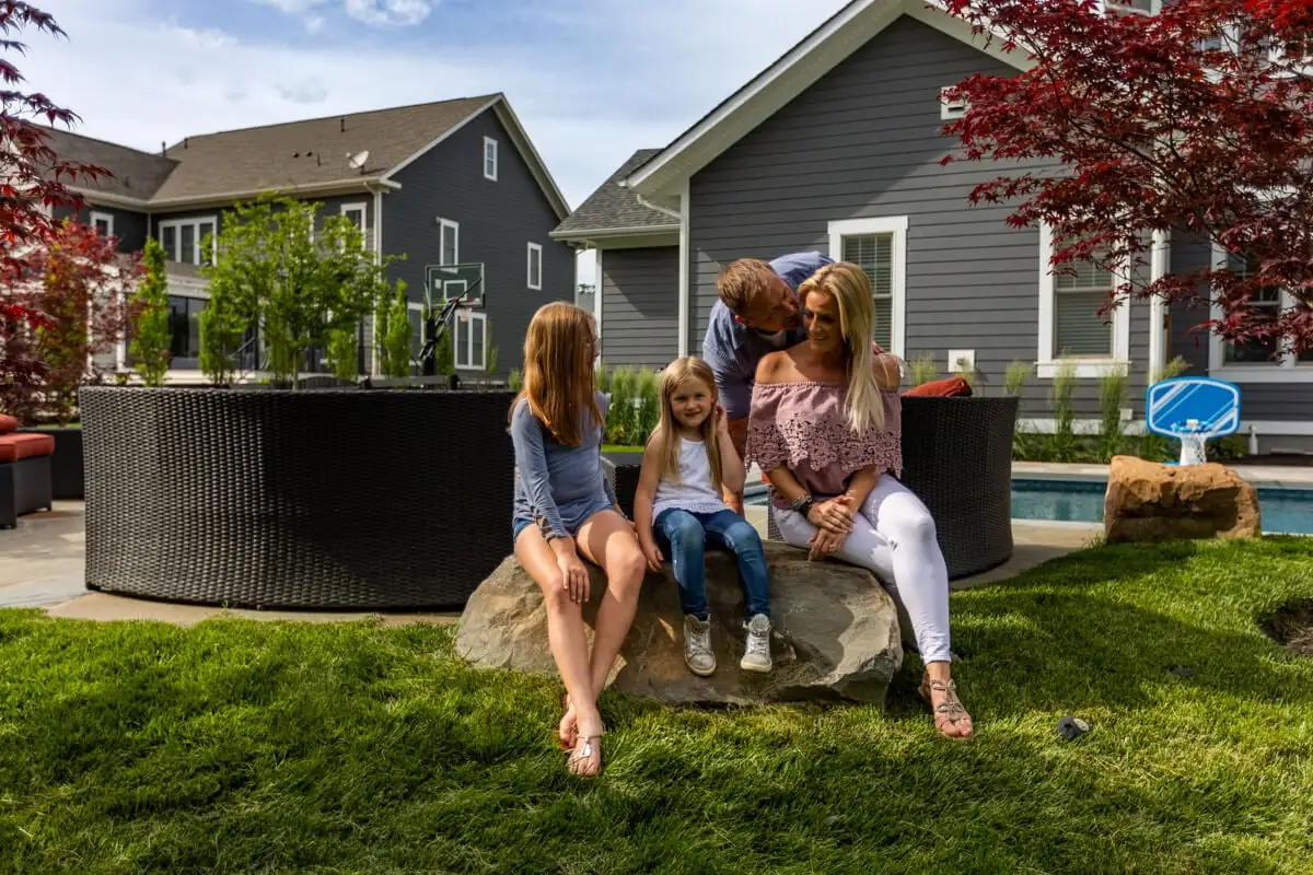 family sits on rock in shady lawn