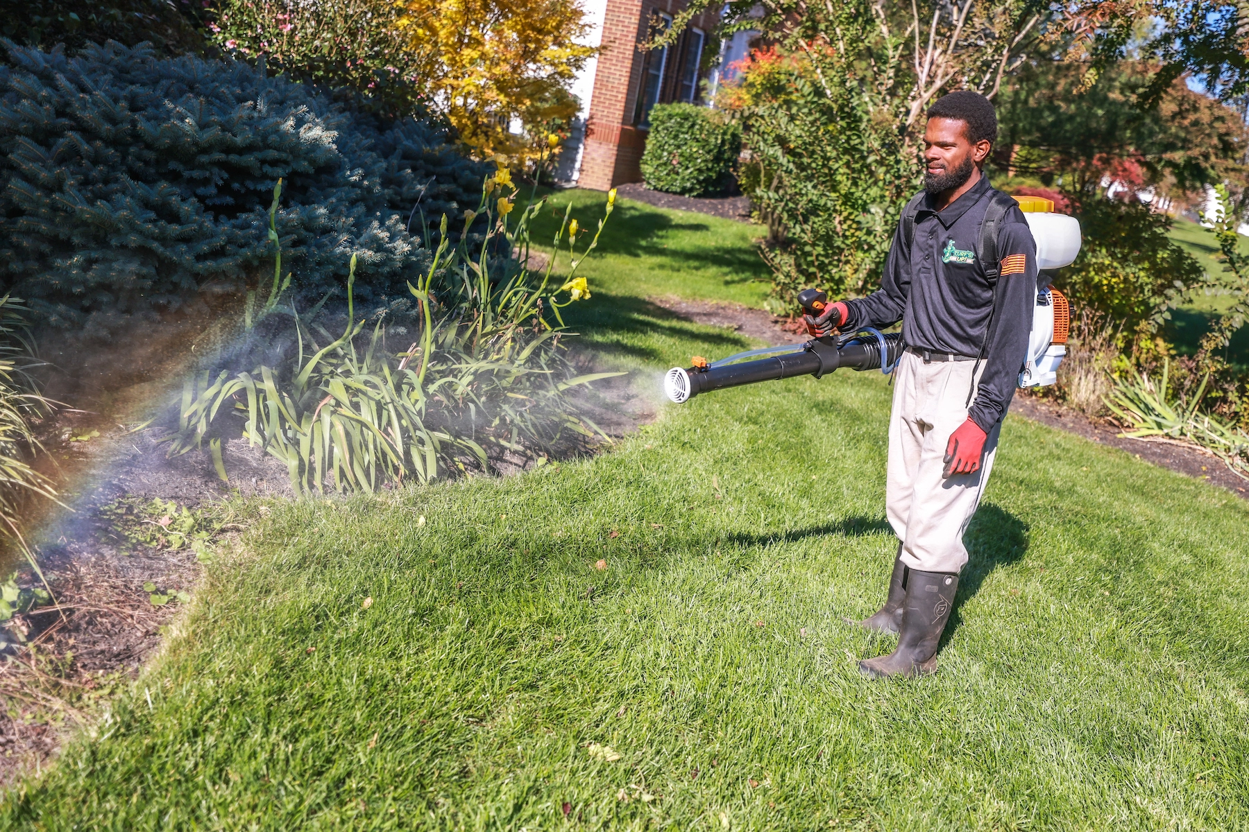 mosquito control technician sprays near landscape bed